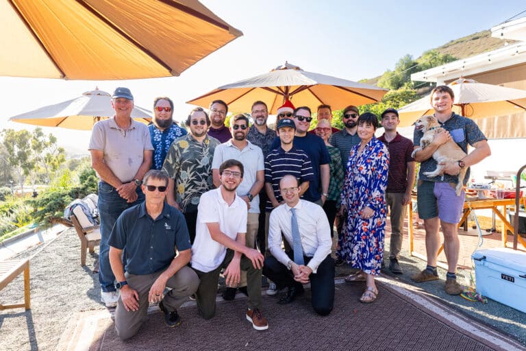 The Clever Ducks team posing together under patio umbrellas, several in Santa hats, one holding a small dog