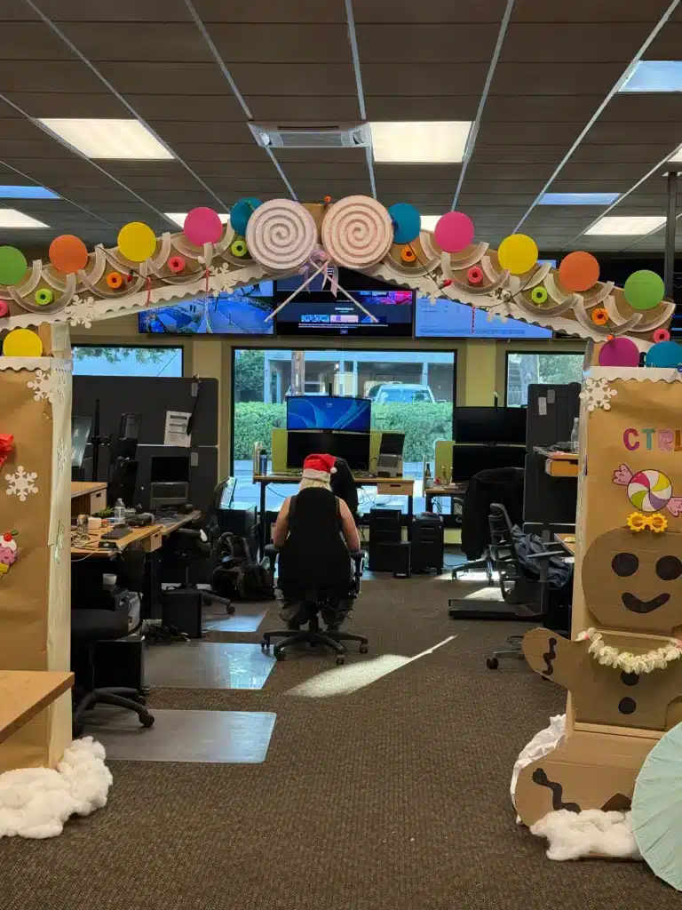 The office decorated with a candy-themed arch and gingerbread cutouts, a technician in a Santa hat at a desk
