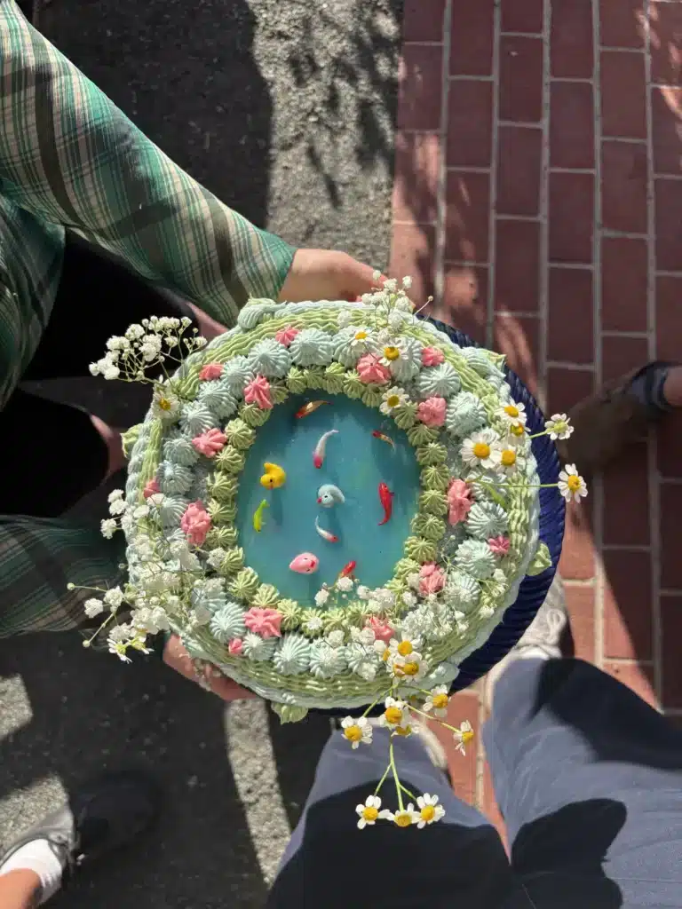 A round cake decorated as a pond with tiny ducks, held in someone's hands