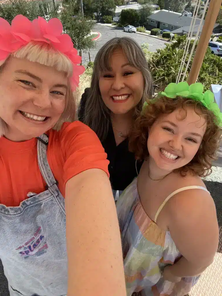 Three team members in flower crowns taking a selfie outdoors