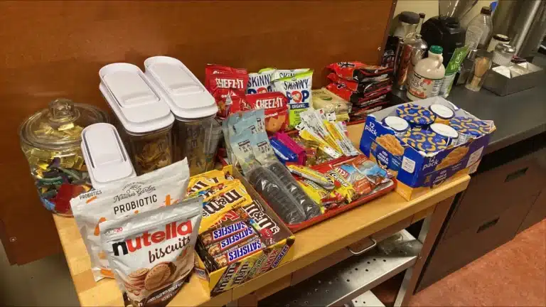 A table stocked with snacks: chips, candy bars, cookies, mac and cheese cups and a jar of wrapped candy